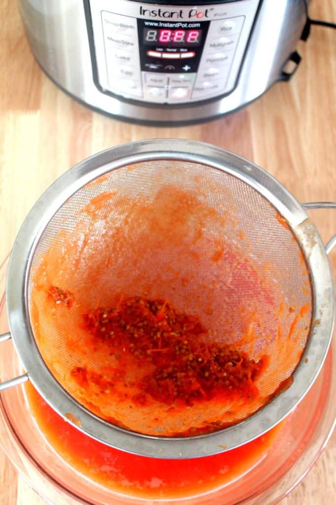Straining blended tomato puree through fine mesh sieve for smooth ketchup