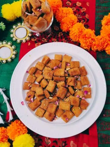 Crispy whole wheat shakarpara diamonds piled on a plate with a cup of chai