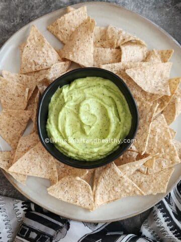 Fresh ingredients for easy avocado dip recipe laid out on a wooden board - ripe avocados, lime, jalapeno, garlic, cilantro, mint, and Greek yogurt