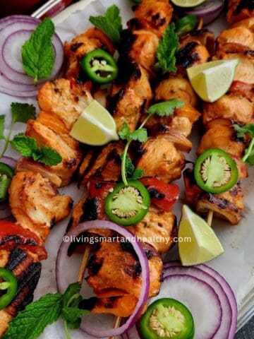 Chicken tikka kebab skewers with charred edges garnished with onion rings and green chutney